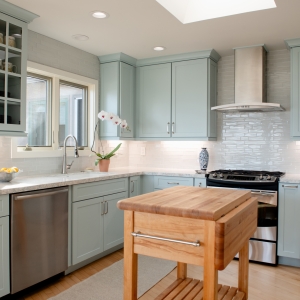 Kitchen view showing blue cabinetry, window over sink, glass-front uppers, and stainless range and hood