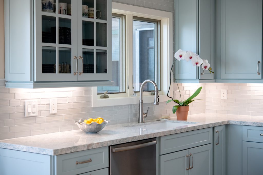 Sink wall with blue cabinets, dishwasher, quartz counters, and white mosaic backsplash