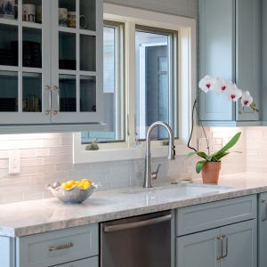 Sink wall with blue cabinets, dishwasher, quartz counters, and white mosaic backsplash