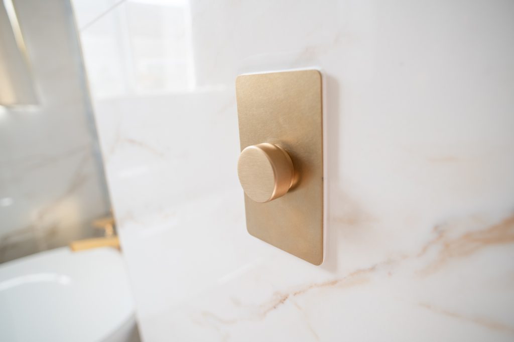 Brass wall plate with a single dimmer knob mounted on a light marble-look wall