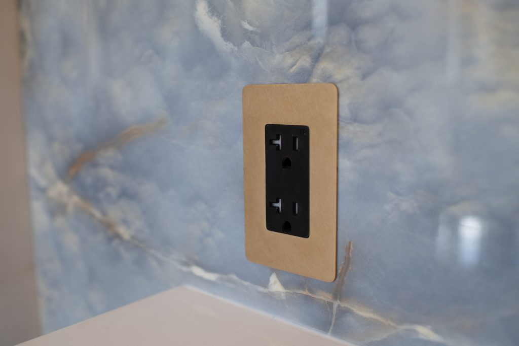 Close-up of a black outlet with a brass faceplate on blue onyx-look tile