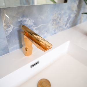 Close-up of a brass bathroom faucet over a white countertop and integrated sink