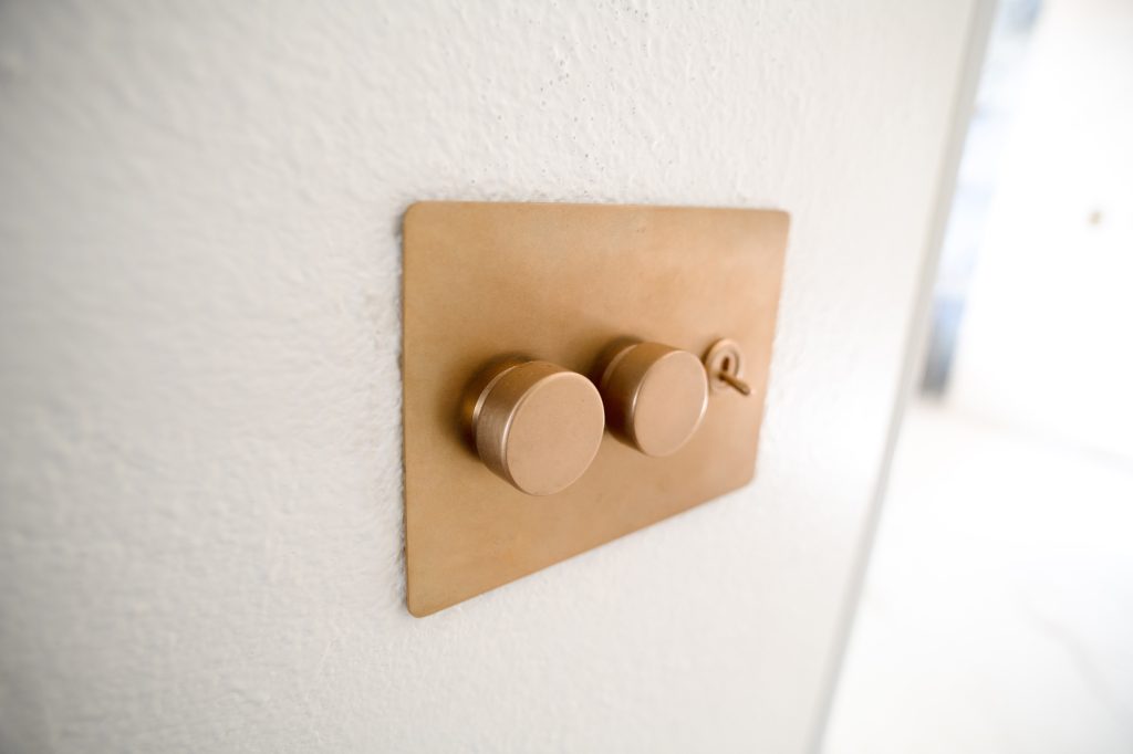 Brass wall plate with two dimmer knobs and a toggle switch on a white wall