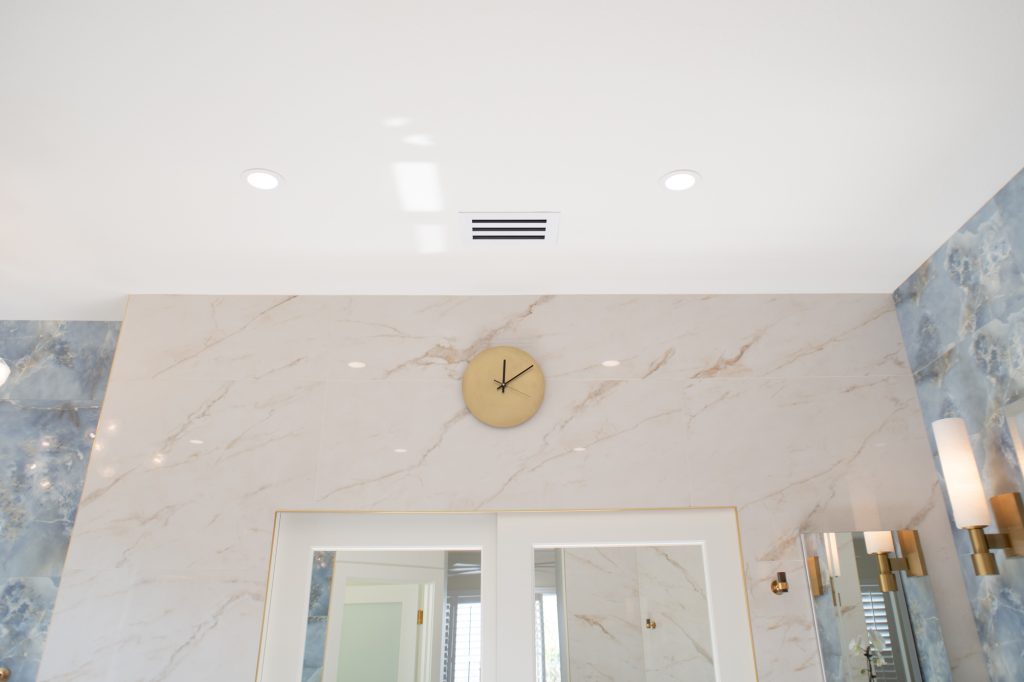 Brass wall clock above marble-look wall tile with recessed ceiling lights