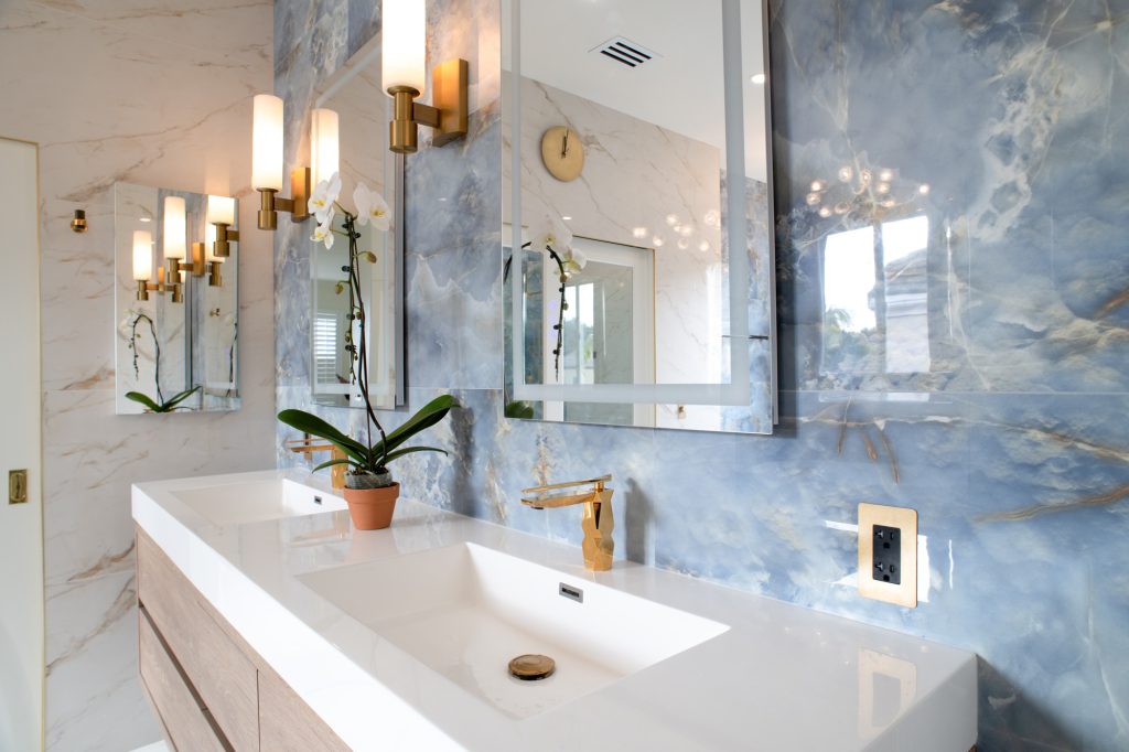 Double vanity with backlit mirrors, brass sconces, and a blue onyx-look tile feature wall
