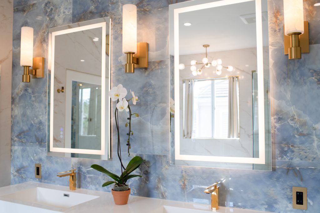 Front view of double vanity with illuminated mirrors and brass sconces on blue tile