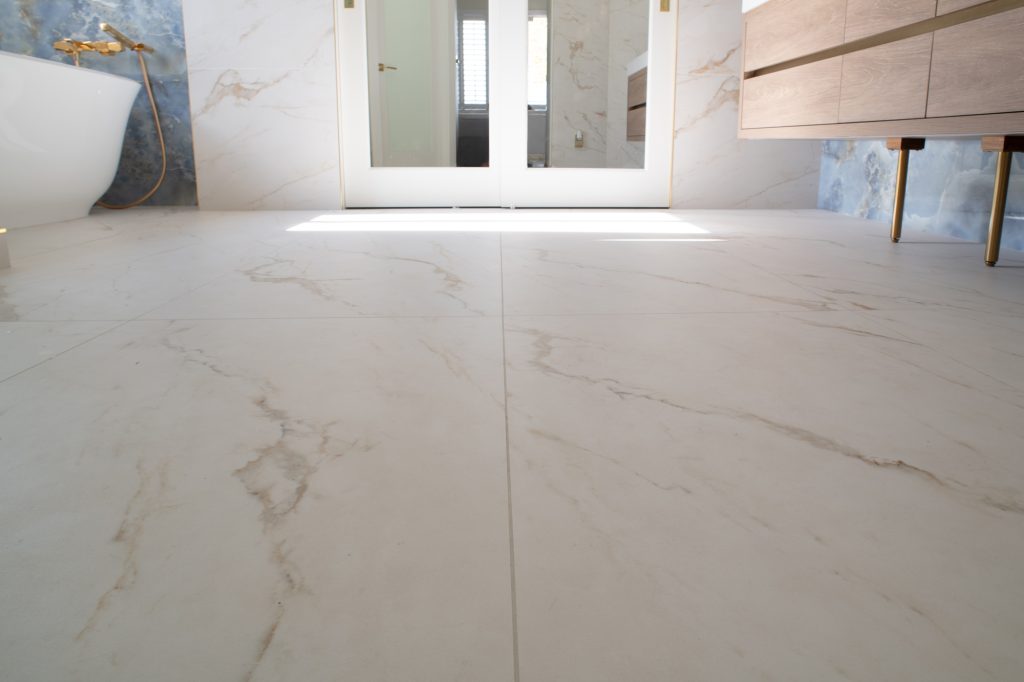 Large-format marble-look floor tiles in a bright bathroom with freestanding tub and floating vanity