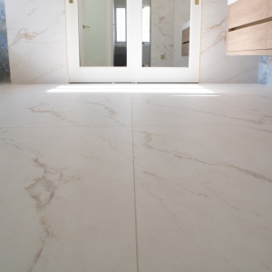 Large-format marble-look floor tiles in a bright bathroom with freestanding tub and floating vanity
