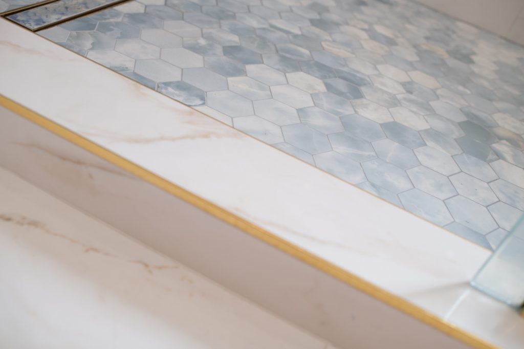 Close-up of shower curb with brass edge and blue hex mosaic tile flooring