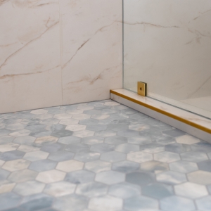 Blue hex mosaic shower floor with glass panel and brass trim detail