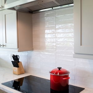 Kitchen induction cooktop, stainless range hood, and glossy white backsplash