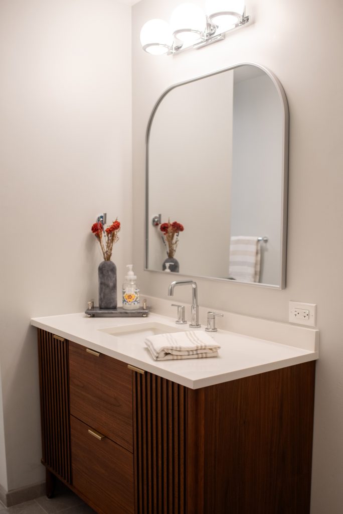 Furniture-style walnut vanity below an arched mirror and a chrome globe light bar