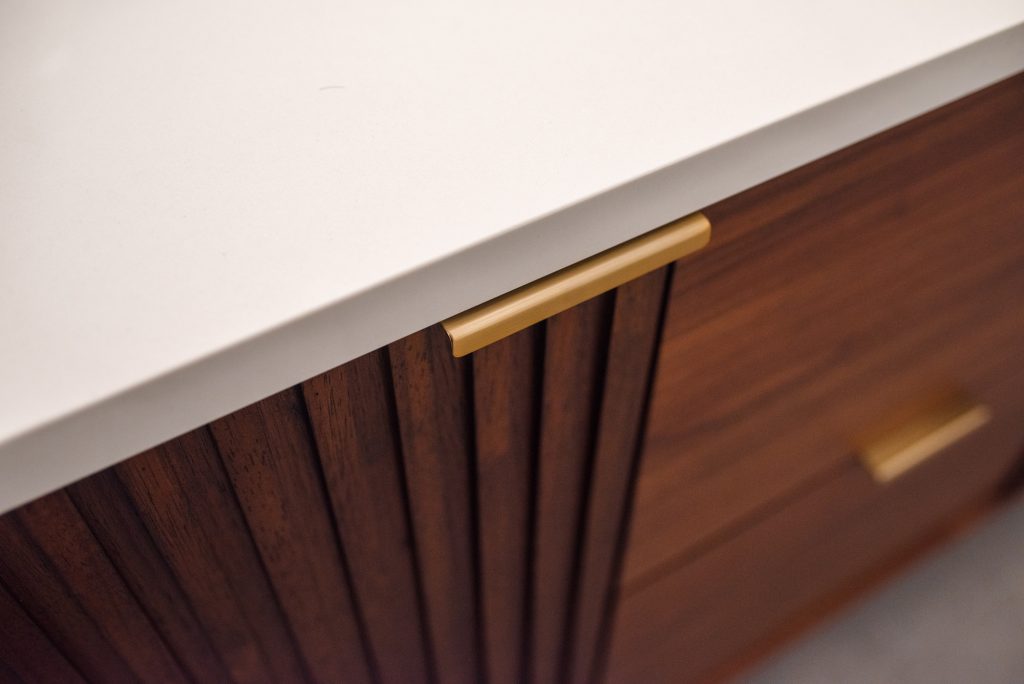 Brass pull and fluted walnut door meeting the white countertop edge