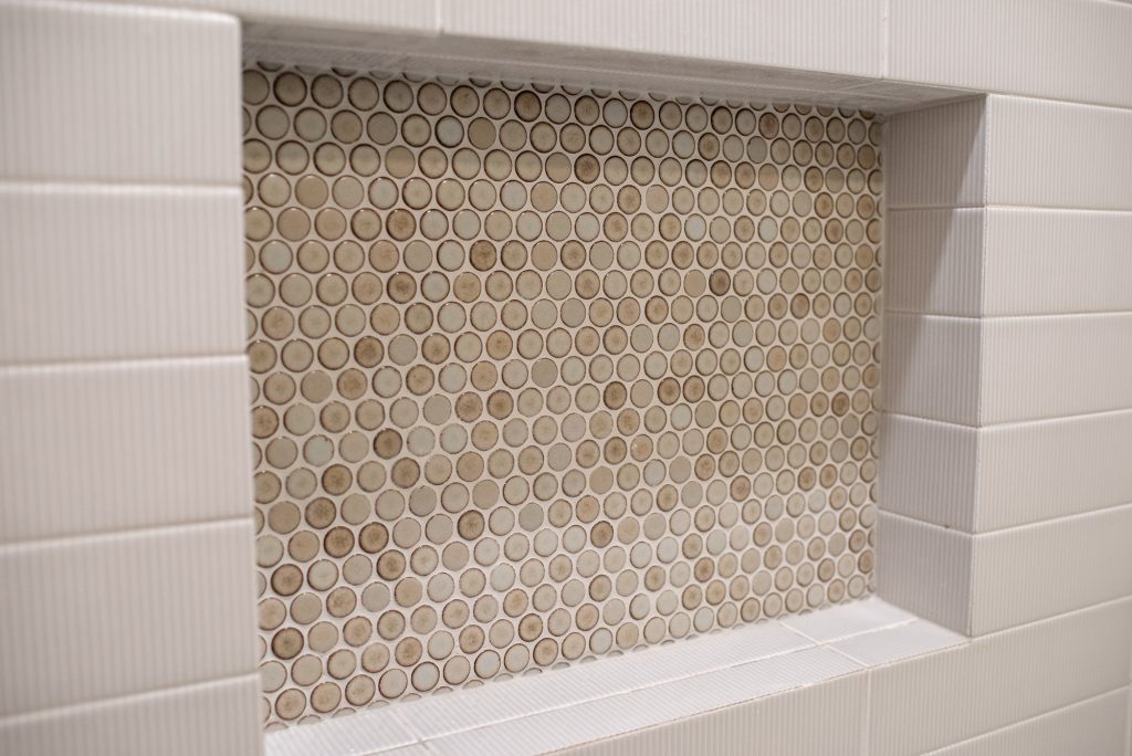 Penny round mosaic in tan and cream filling the niche, ribbed white tile around it