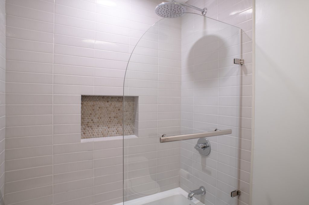 Tub surround in white stacked tile with a penny round niche and a chrome rain head