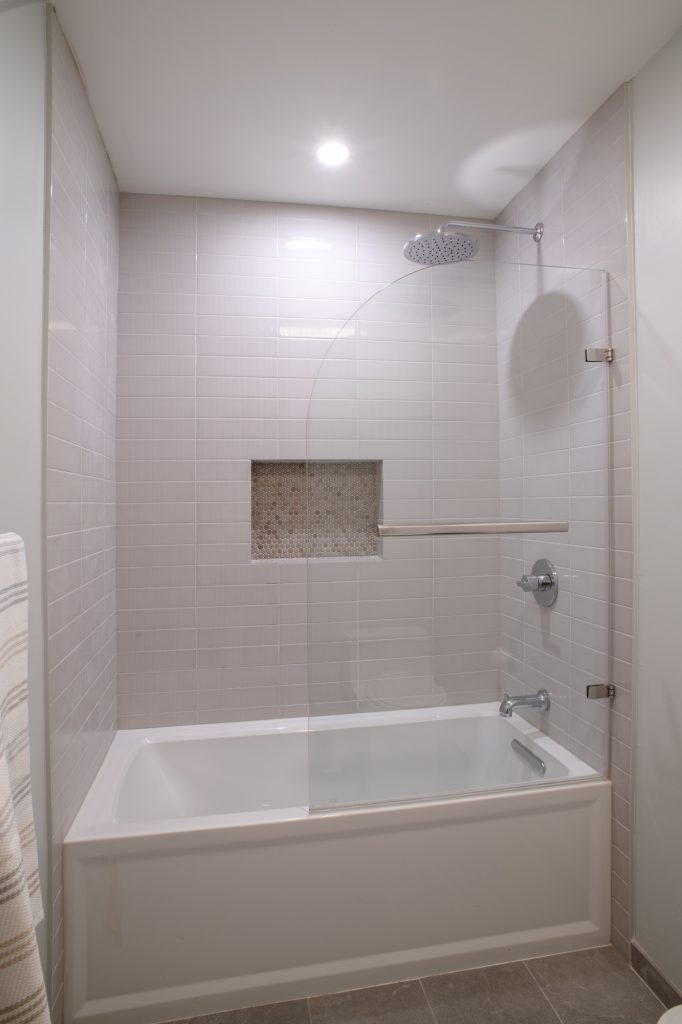 Alcove tub with a curved frameless glass panel that swings clear of the opening