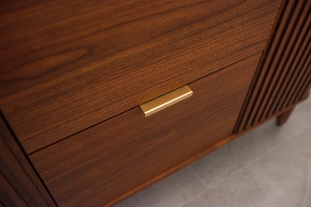 Walnut drawer front with a slim brass pull, fluted panel and tapered leg alongside