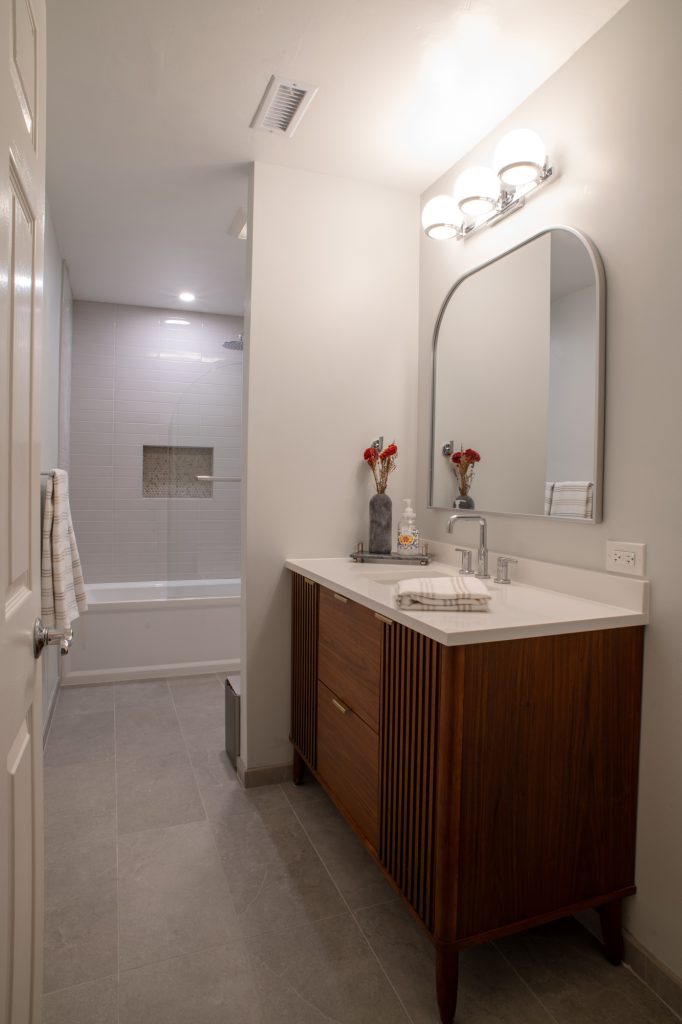 Fluted walnut vanity with an arched mirror, alcove tub and shower beyond the partition wall