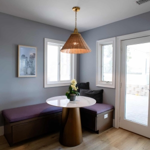 Built-in banquette with storage benches, a round marble-look table, and a woven rattan pendant beside the patio doors
