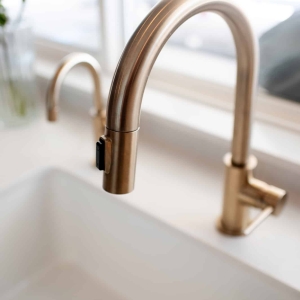 Two champagne bronze faucets at the white farmhouse sink