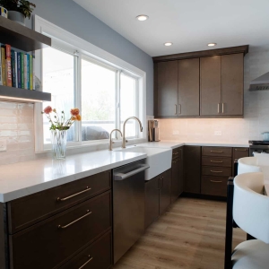 Farmhouse apron-front sink below the window with floating shelves and quartz counters