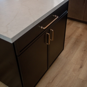 Corner of the black island showing the quartz countertop edge and brass cabinet pulls