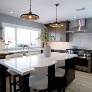 Quartz-topped island on a black base with white upholstered stools under two brass and black pendants