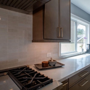 Range wall with the ceramic tile backsplash, a wood hood surround, and a coffee station by the window