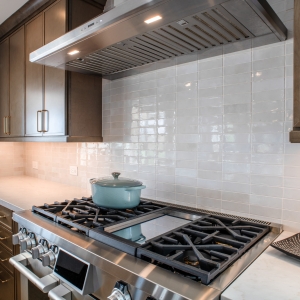 SKS dual fuel range with integrated griddle beneath a stainless hood and glossy ceramic backsplash
