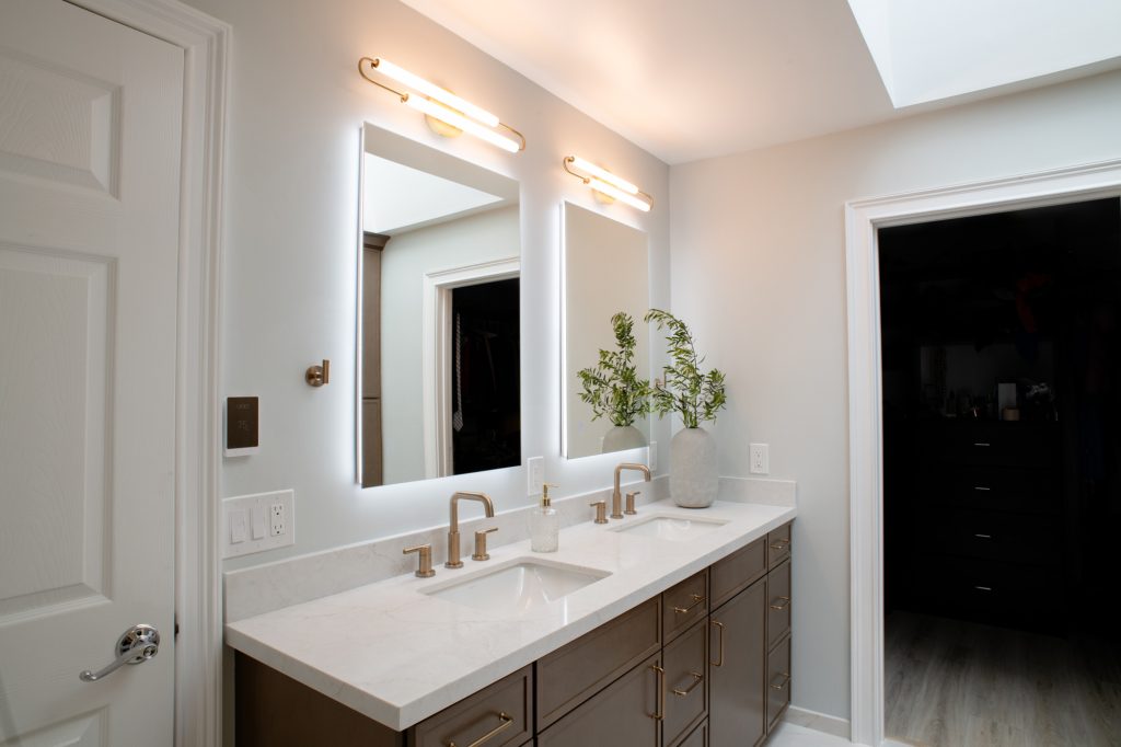 Double vanity with two backlit LED mirrors and brass linear sconces, seen from the doorway