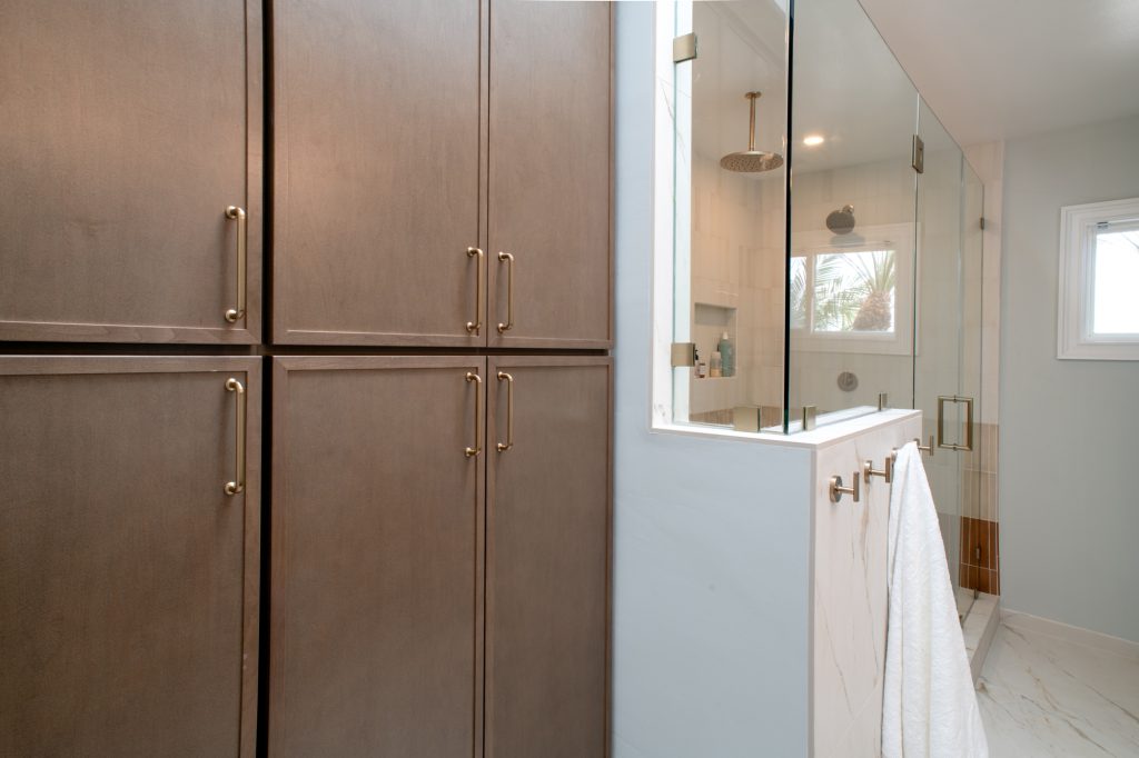 Floor-to-ceiling linen tower beside the walk-in shower, with towel hooks on the pony wall