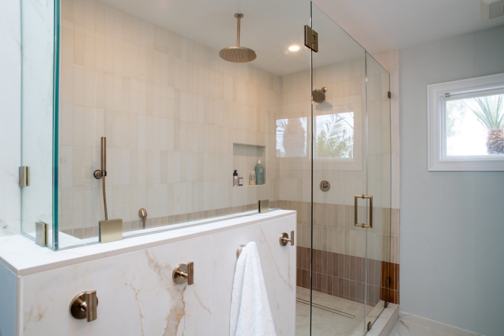 Walk-in shower behind a pony wall capped in Calacatta Oro porcelain, frameless glass above