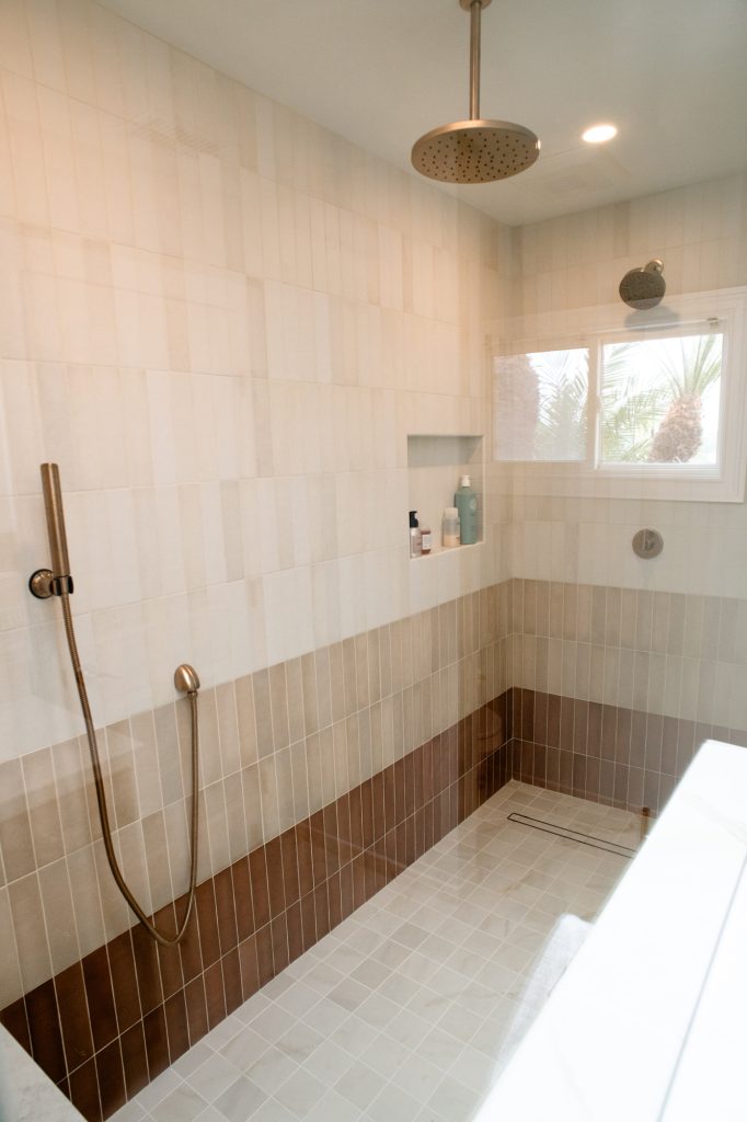 Inside the shower, ceiling-mounted rain head above a tiled niche and a linear floor drain