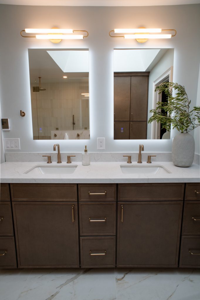 Vanity seen straight on, two arched-arm sconces above backlit mirrors, skylight overhead