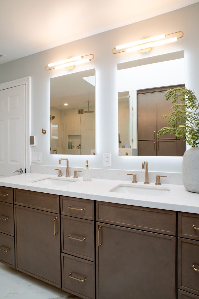 Quartz-topped vanity with the shower and linen tower reflected in the two lit mirrors