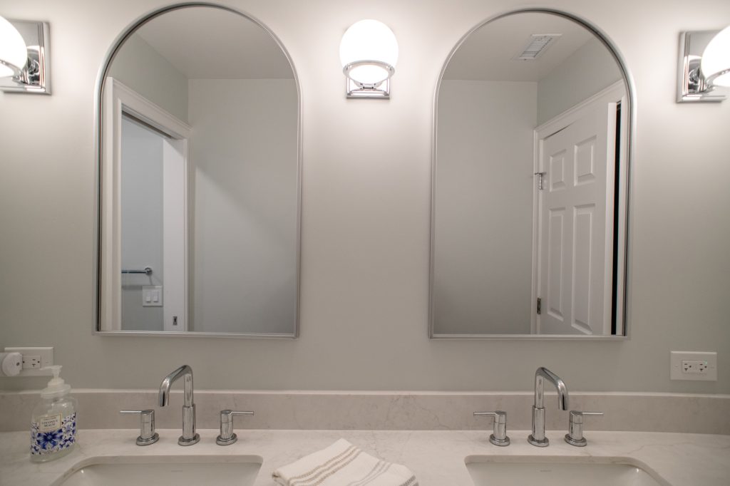 Paired arched mirrors flanking a chrome globe sconce above the counter