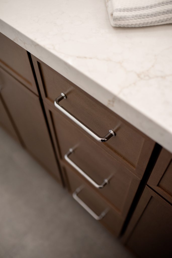 Chrome pull on a drawer front, quartz counter and gray floor tile beyond