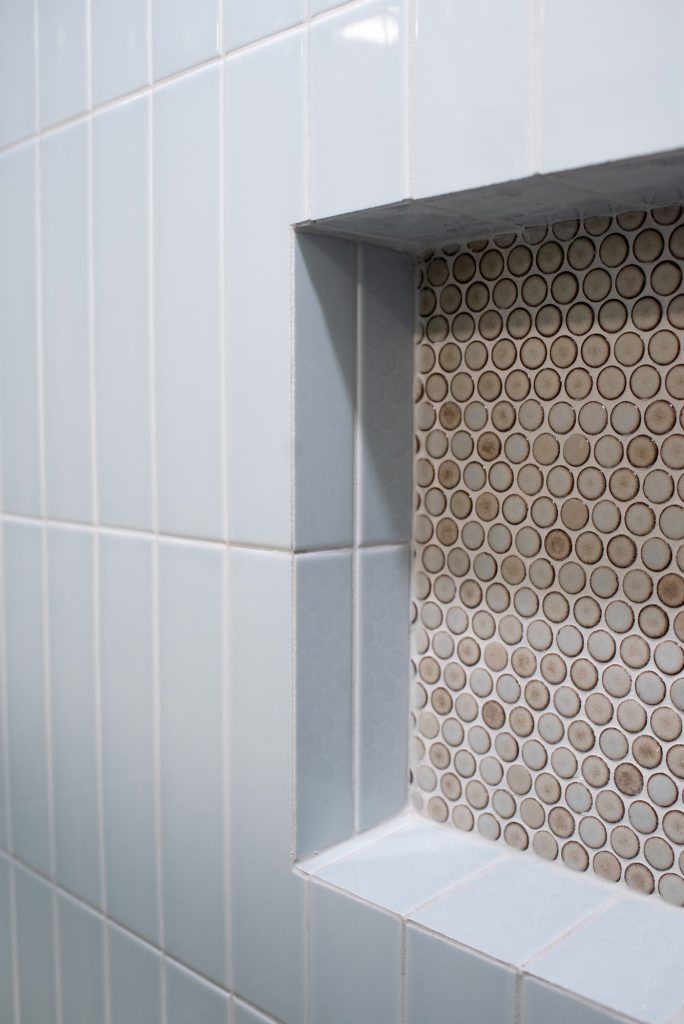 Recessed niche lined in penny round mosaic, framed by pale blue stacked tile