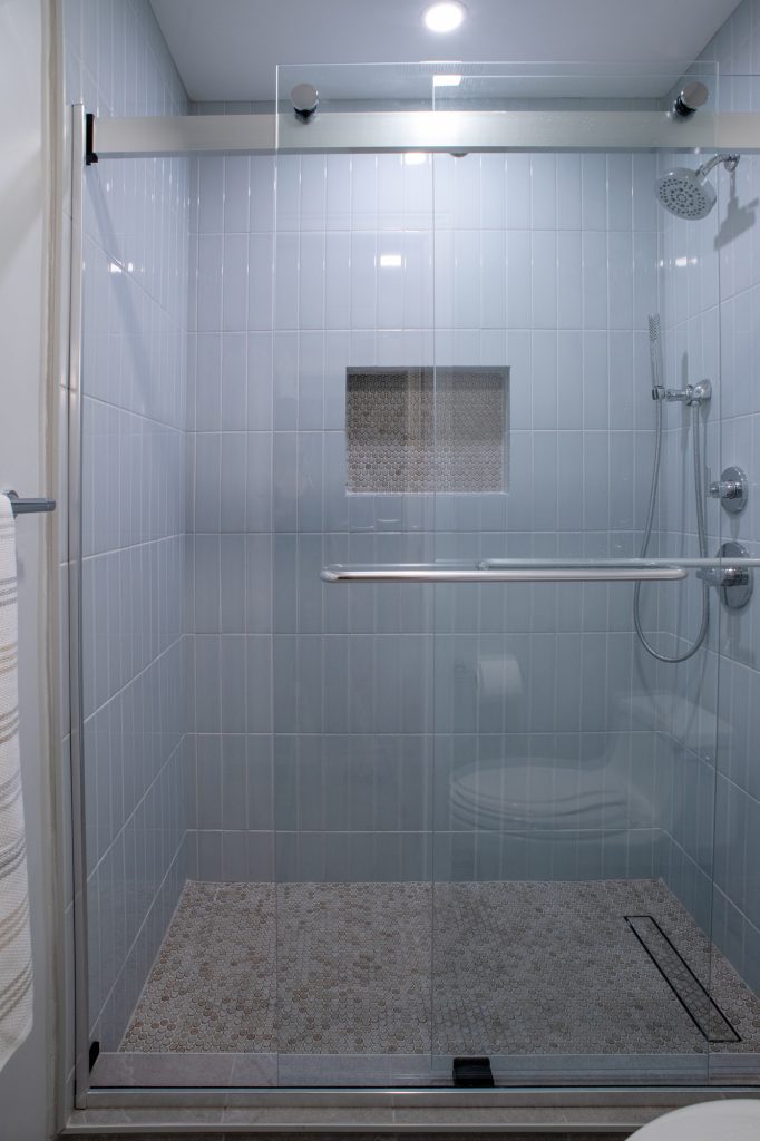Shower in its own compartment, pale blue vertical tile and a penny round mosaic floor