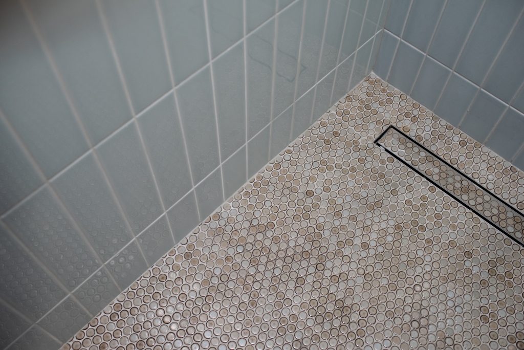 Corner of the shower where the vertical wall tile meets the penny round floor and drain