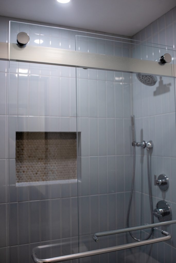 Bypass shower door on its track, niche and chrome controls visible through the glass