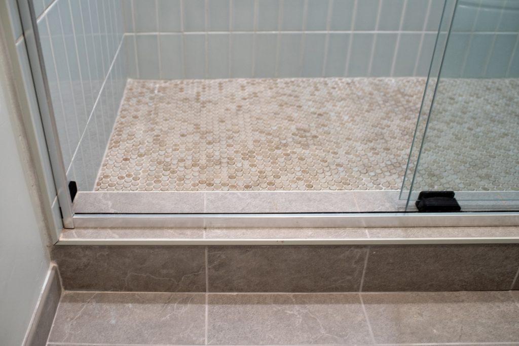 Shower threshold where the penny round floor meets the large-format gray tile outside