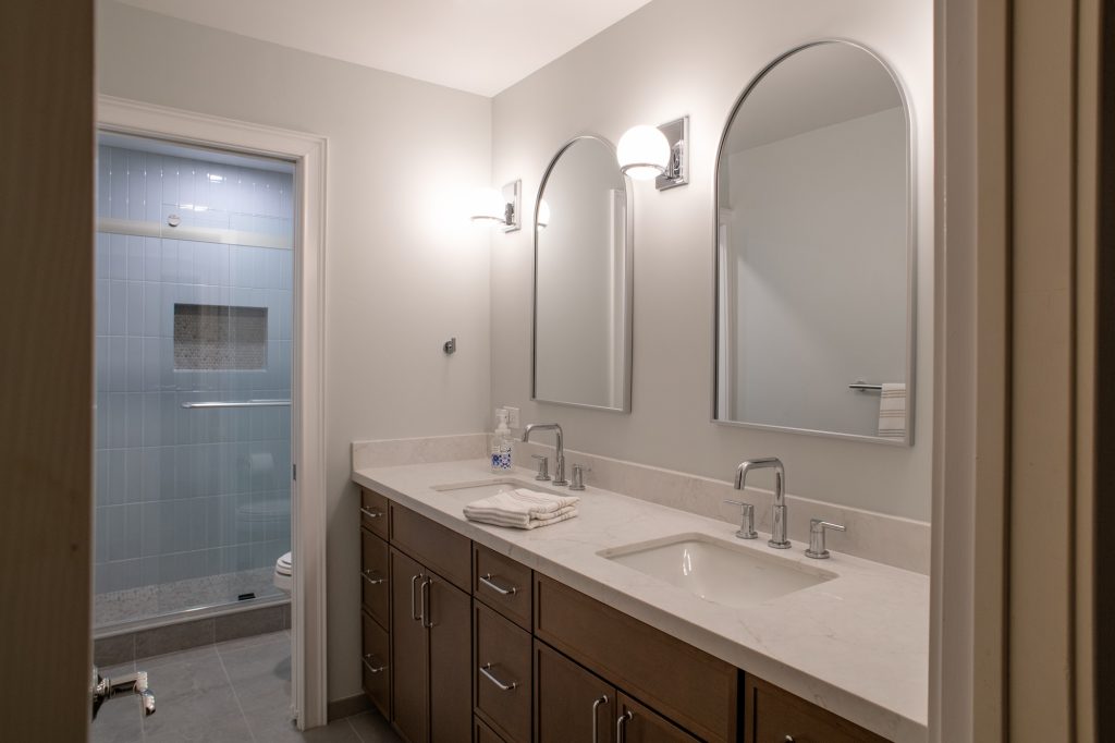 Double vanity under two arched mirrors, with the shower compartment through the doorway