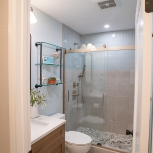 The bathroom seen through its doorway: vanity, toilet, and tiled shower with a pebble floor