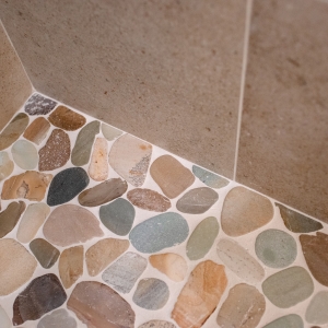 Corner where the Waterbrook sliced pebble shower pan meets the speckled beige wall tile