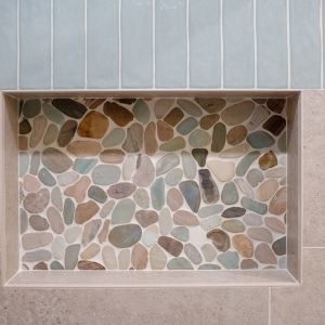 Recessed shower niche lined with multicolored pebble mosaic, its top edge at the tile change