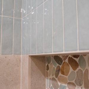 Angled view of undulated blue ceramic stacked vertically over the porcelain, niche edge below