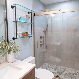 Hall bathroom with a wood vanity, glass wall shelves, and a walk-in shower behind sliding glass
