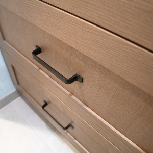 Matte black pulls on the straight-grained wood drawers of the vanity