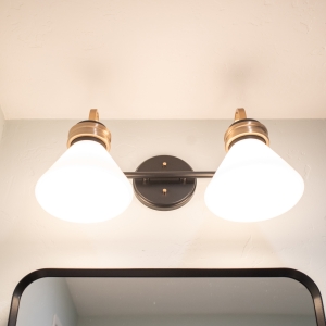 Two-light vanity fixture with cone shades in bronze and brass above the mirror frame